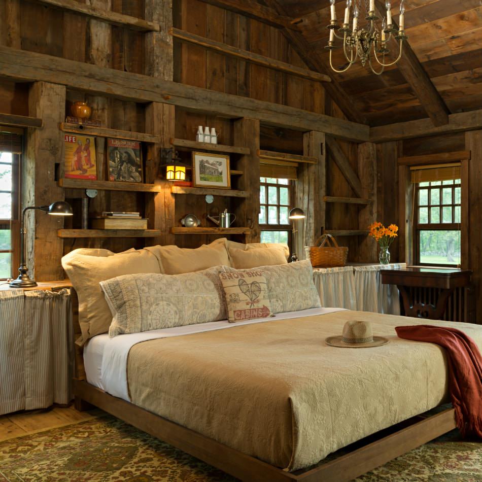 Rustic wood room with several windows, open shelves with collectibles, and large bed with tan bedding