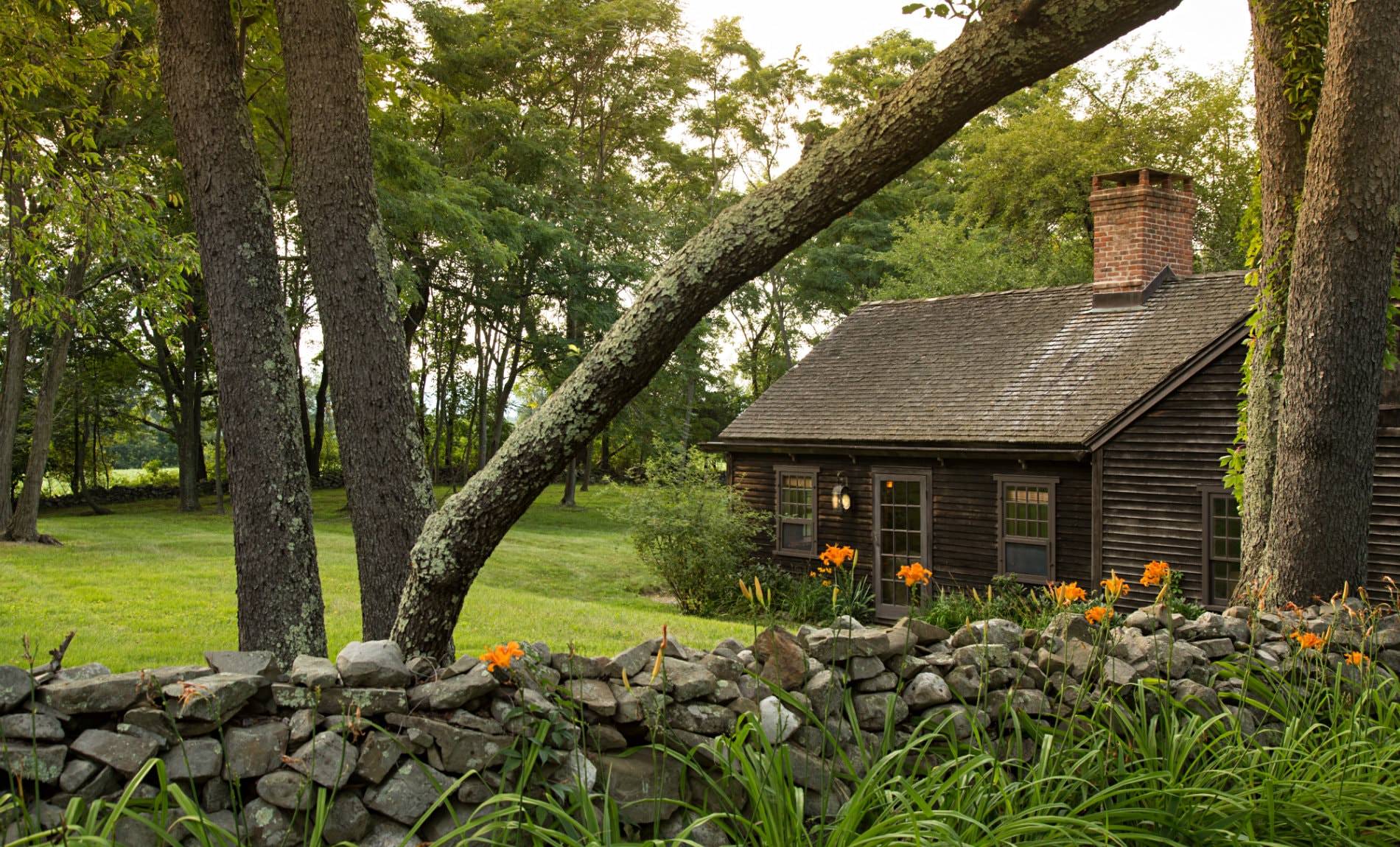 Rustic brown cabin surrounded by green grass, a gray stone wall and trees