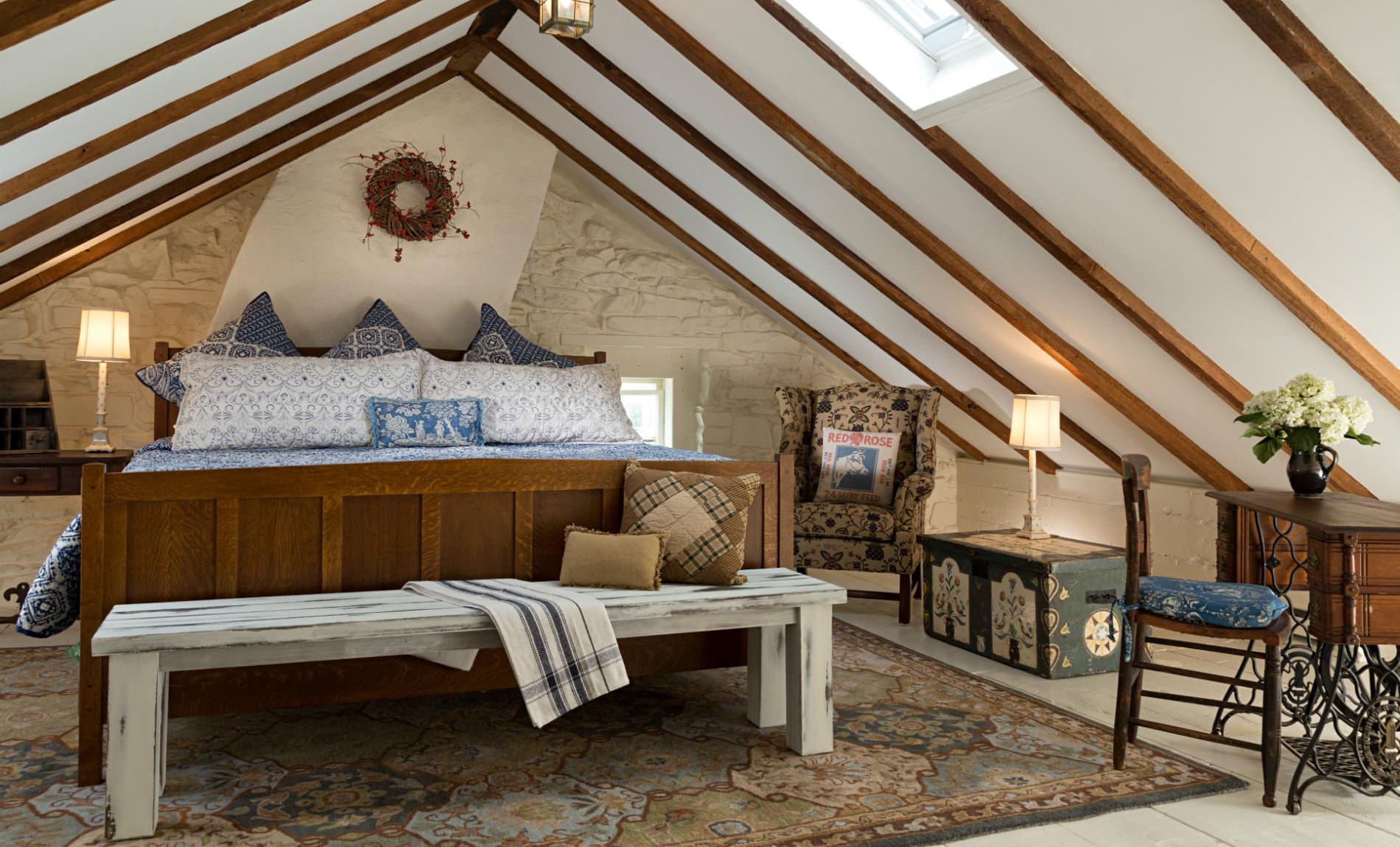 Vaulted attic room with one white stone wall, large wood bed with blue and white bedding, and wood floors