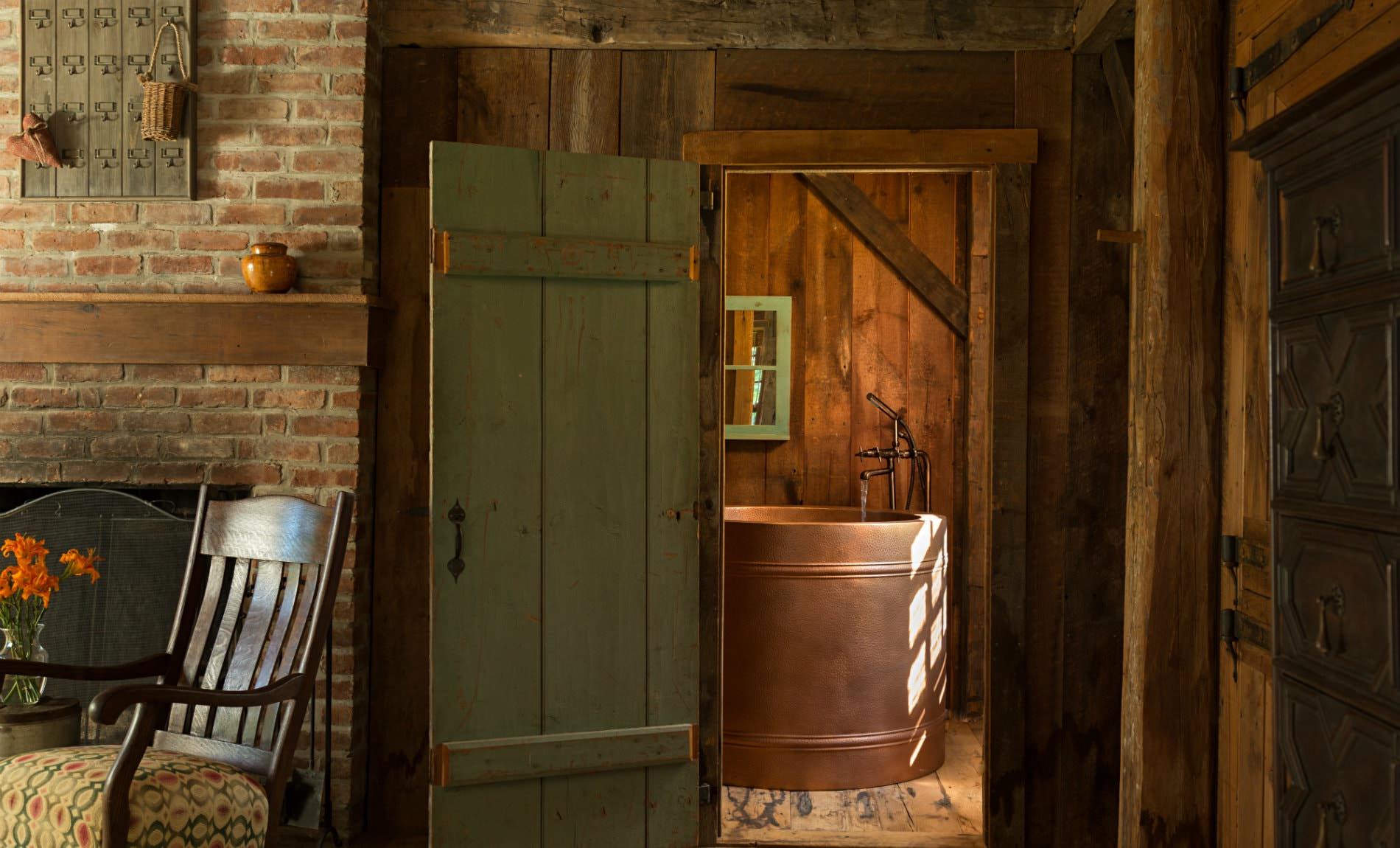 Rustic wood and brick room with view of round copper tub through an open green door