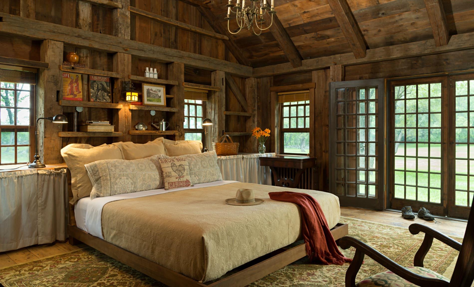 Vaulted rustic wood plank room with exposed beams, double-hung windows and French door, and large bed with tan bedding