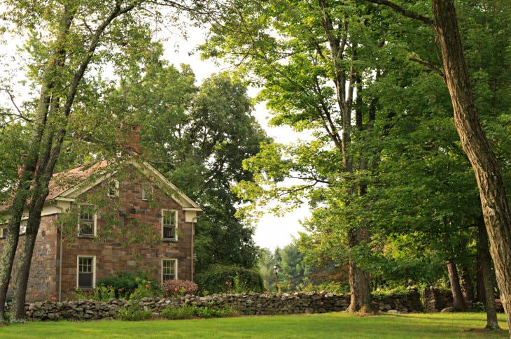 Brown stone building and stone wall running along property surrounded by green grass and trees