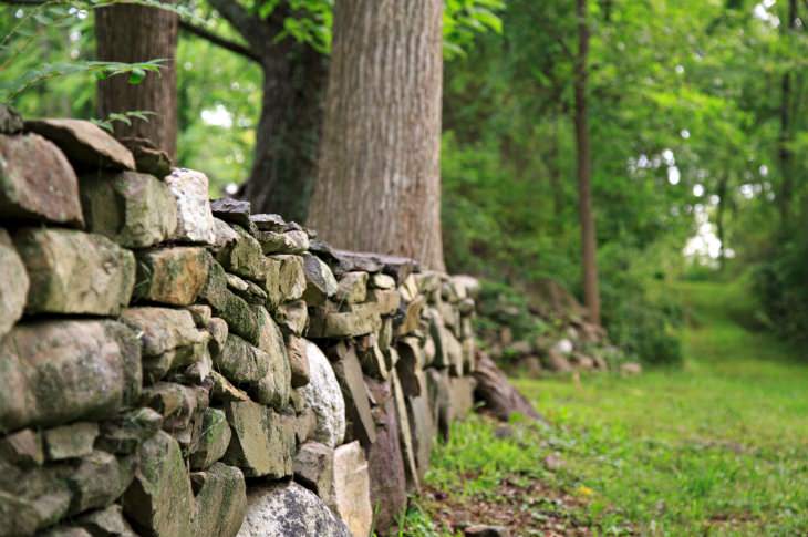 Low gray stone wall surrounded by green grass and trees