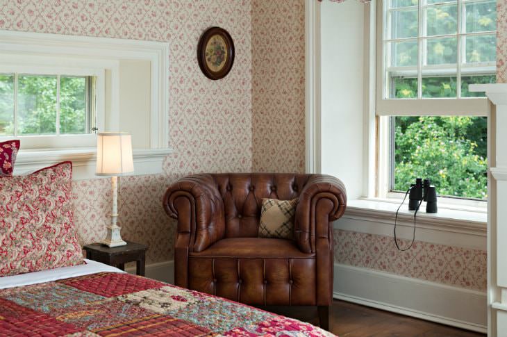 Cozy room with red and white papered walls, deep window sill with binoculars, red quilted bed and brown leather chair