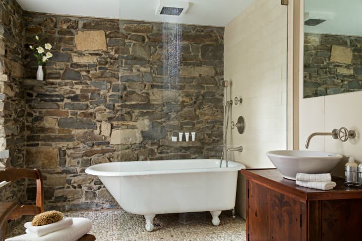 Stone and wood walls, claw foot tub with rain shower head and glass door, vanity with white vessel sink
