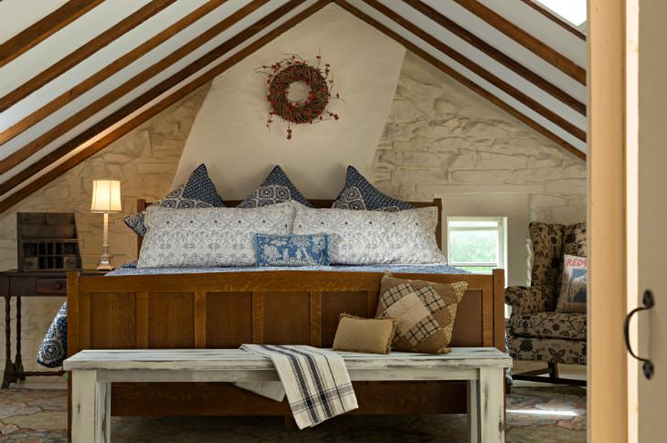 Large wood bed with blue and white bedding against a white stone wall under vaulted ceiling with exposed beams