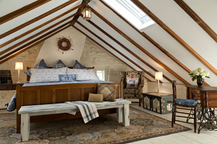 Vaulted attic room with one white stone wall, large wood bed with blue and white bedding, and wood floors