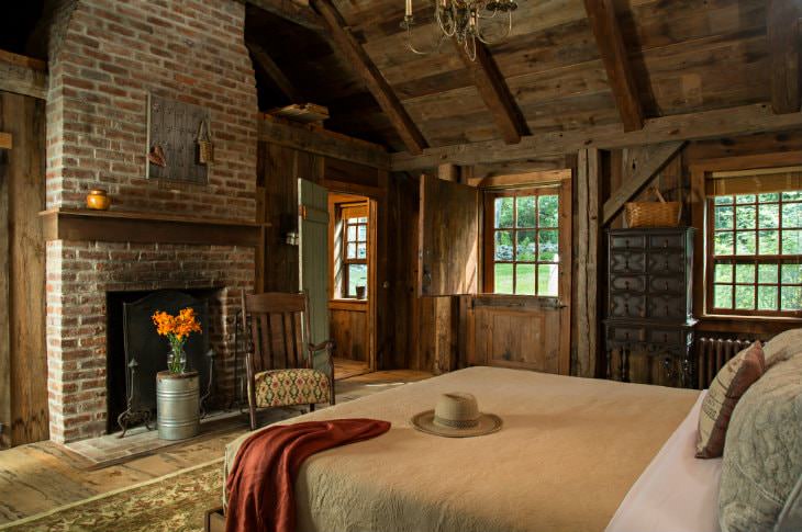 Cozy rustic room with wood floor and walls, vaulted wood ceiling, brick fireplace, double hung windows and large bed