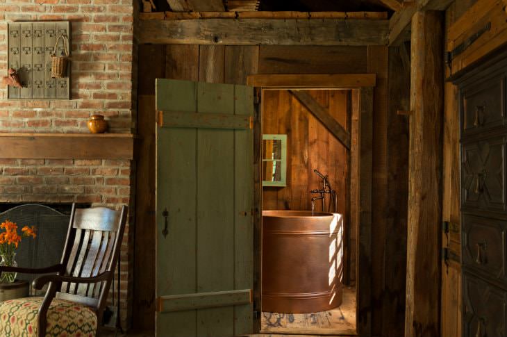 Rustic wood and brick room with view of round copper tub through an open green door