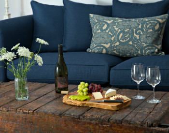 Blue sofa and rustic coffee table topped with fresh white flowers, cheese board with fruit, wine bottle and wine glasses