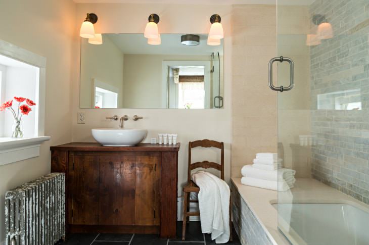 White bathroom with dark tile floor, rustic wood vanity with modern white sink, large mirror and sconce lighting