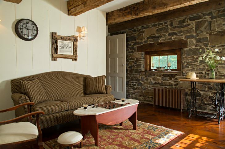 Rustic sitting room with white painted wood walls, stone wall with small window, sofa and chair around painted coffee table