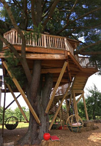 Large wood treehouse with railing and stairs and green basket swings