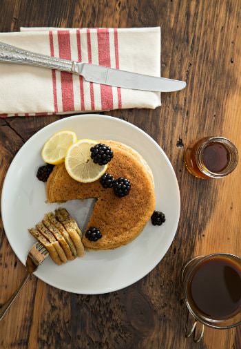 Table topped with a white plate of pancakes and fresh berries, a cup of coffee and cup of maple syrup