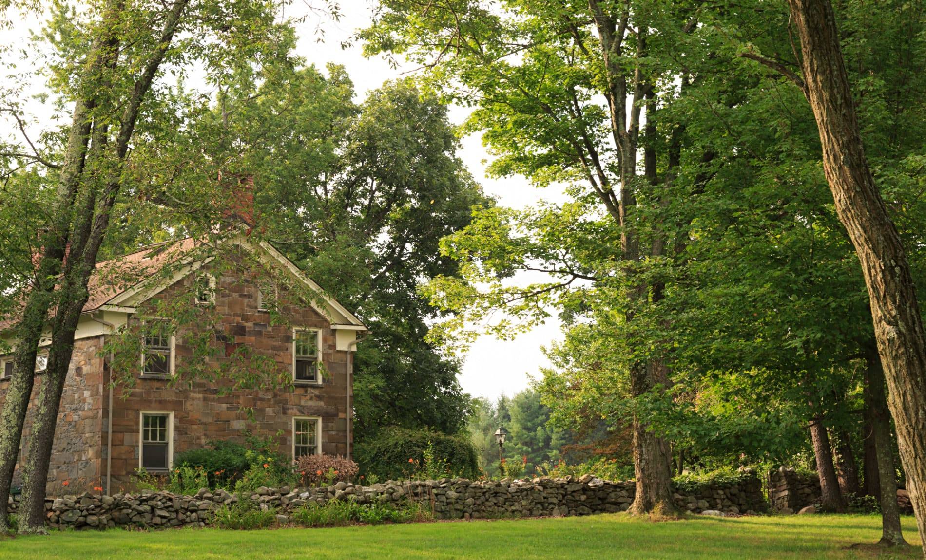 Brown stone building and stone wall running along property surrounded by green grass and trees