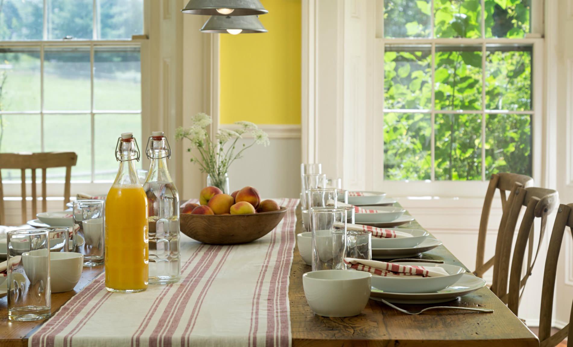 Table set with white plates and cups, bowl of fruit, vase of fresh flowers and bottles of juice and water